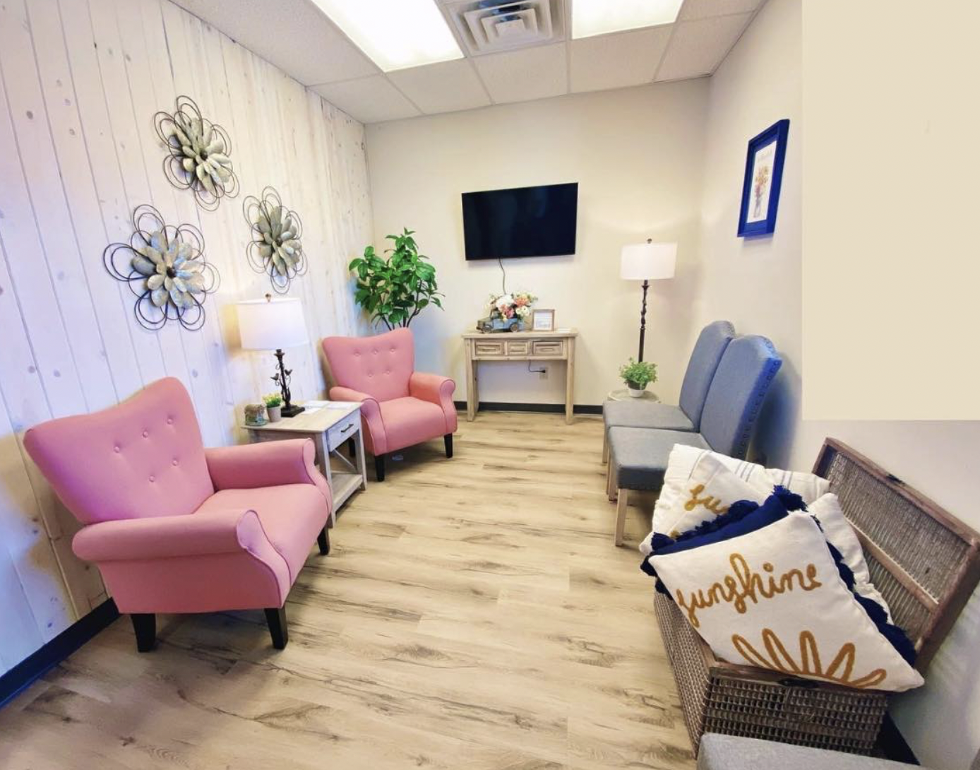 MomDoc Women for Women Show Low living-room with pink armchairs, blue chairs, and mounted TV